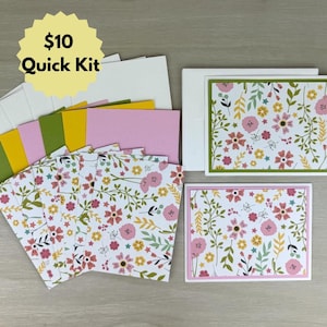 May include: A craft kit with floral patterned cards, envelopes, and colored paper. The cards feature pink, yellow, and green floral designs. The kit includes the text "$10 Quick Kit" in a yellow burst.