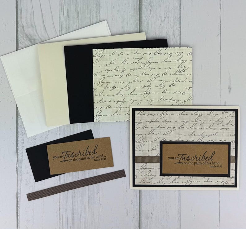 May include: A collection of stationery items, including cards, envelopes, and tags. The cards feature a script-like pattern and the word "Inscribed" with the text "you are on the palm of his hand..." in a brown rectangle.