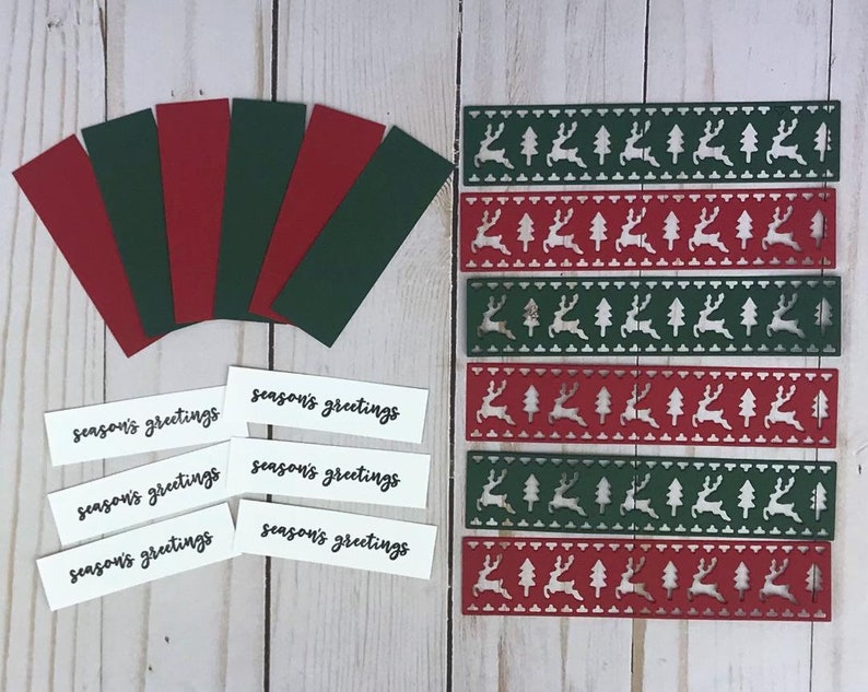 以下が含まれることがあります： 赤と緑のカードストックの長方形のストリップ6枚、黒い文字でseason's greetingsと印刷された白い長方形のラベル6枚、トナカイと木の模様が繰り返されるダイカットストリップ6枚を含むクラフト用品のセット。