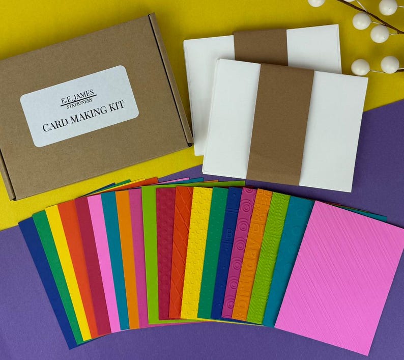 May include: A card making kit with a brown box and a label that reads "CARD MAKING KIT". The kit includes white cardstock, brown paper bands, and a variety of colorful cardstock in various textures and patterns. The background is yellow and purple.