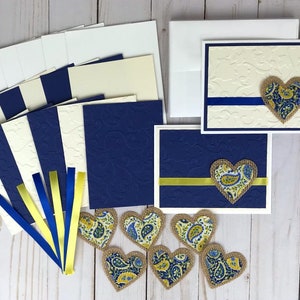 May include: A collection of handmade greeting cards and embellishments. The cards feature embossed designs and are accented with blue and yellow ribbons and paisley heart-shaped appliqu&eacute;s. Includes envelopes and blank cardstock.