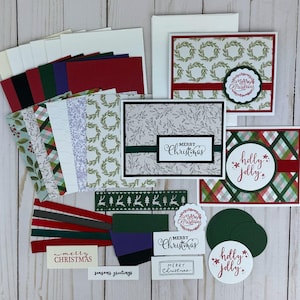 May include: A collection of Christmas-themed greeting cards and paper crafting supplies featuring wreaths, plaid patterns, and botanical prints. The set includes envelopes, cardstock strips in red, green, and black, and labels with Merry Christmas text.