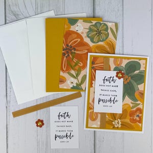 May include: A stationery set featuring floral-patterned cards, envelopes, and embellishments. The cards have a cream background with orange, green, and yellow flowers. The text "faith does not make things easy, it makes them possible" is printed on a card.