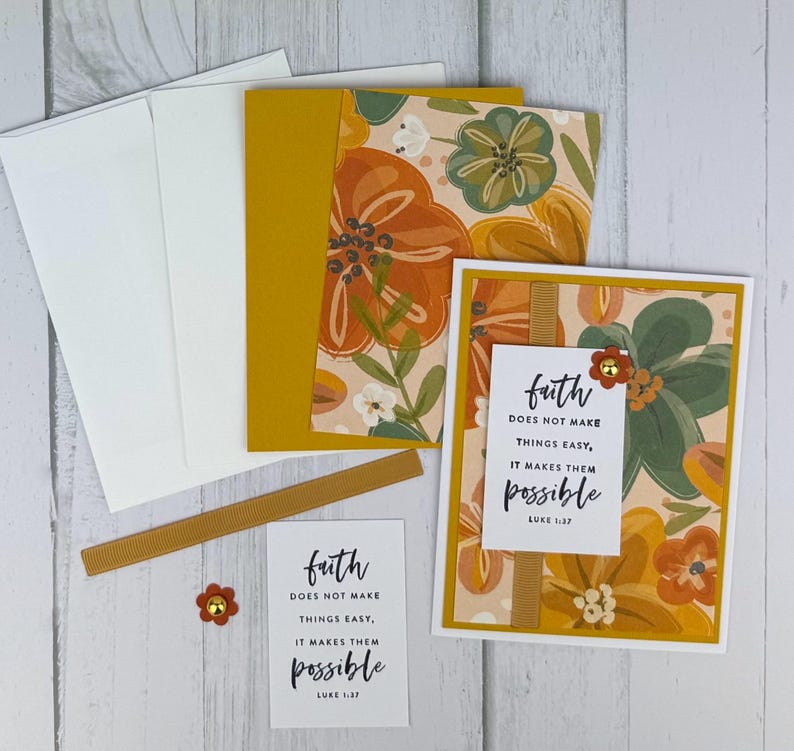 May include: A stationery set featuring floral-patterned cards, envelopes, and embellishments. The cards have a cream background with orange, green, and yellow flowers. The text "faith does not make things easy, it makes them possible" is printed on a card.