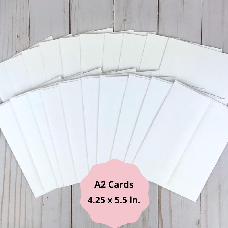May include: A stack of white A2 cards, each measuring 4.25 x 5.5 inches, arranged on a light wood surface. The cards are blank and ready for use. A pink label at the bottom displays the card size.