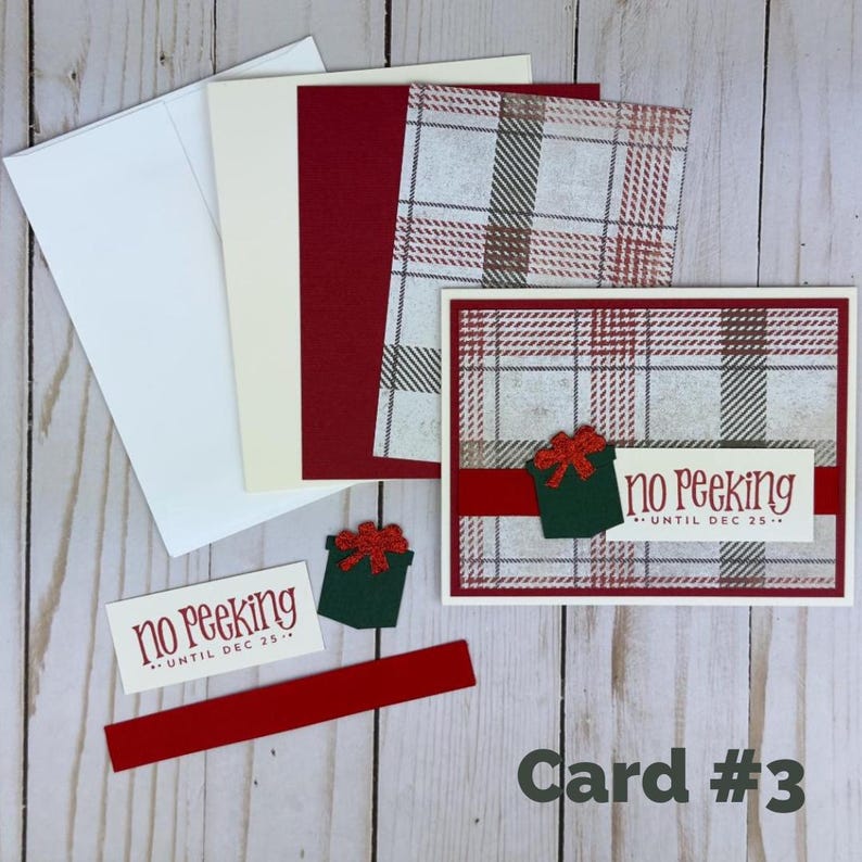 Puede incluir: Un juego de tarjetas de felicitaci&oacute;n con un sobre blanco, una hoja de cartulina crema, una hoja de cartulina roja y papel a cuadros. La tarjeta principal muestra un dise&ntilde;o de cuadros rojos y grises con un icono de regalo verde y el texto no peeking until dec 25.