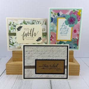 May include: Three handmade greeting cards with inspirational quotes. One card features the text "faith" and "2 Corinthians 5:7". Another card has the text "be still and know" and "Psalm 46:10". The third card has the text "you are inscribed" and "Isaiah 49:16".