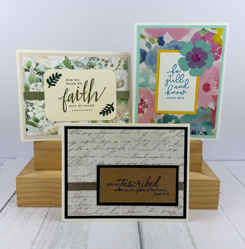 May include: Three handmade greeting cards with inspirational quotes. One card features the text "faith" and "2 Corinthians 5:7". Another card has the text "be still and know" and "Psalm 46:10". The third card has the text "you are inscribed" and "Isaiah 49:16".