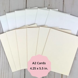 Puede incluir: Un conjunto de tarjetas A2 de color crema que miden 10,8 x 14 cm, dispuestas en forma de abanico, acompa&ntilde;adas por un juego a juego de sobres blancos lisos colocados directamente detr&aacute;s de las tarjetas en una formaci&oacute;n superpuesta.