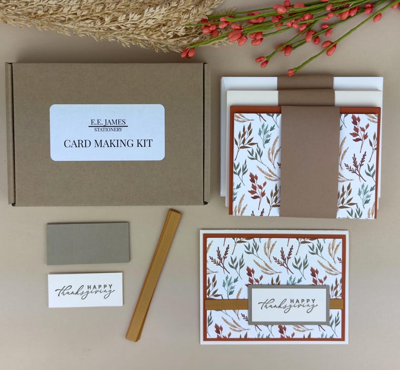 May include: A card making kit in a brown cardboard box labeled E.E. JAMES STATIONERY CARD MAKING KIT. Includes stacks of cards with autumn leaf patterns, brown paper bands, a gold strip, a gray rectangle, and a white label reading HAPPY THANKSGIVING.