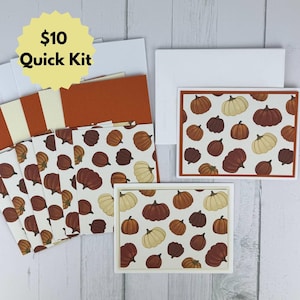 May include: A stationery set featuring a pattern of various pumpkins in shades of orange, brown, and cream. The set includes multiple folded cards and matching white envelopes. A yellow starburst graphic in the top left corner displays the text $10 Quick Kit.