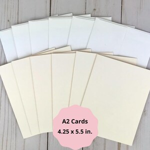 May include: A collection of A2 cards, measuring 4.25 x 5.5 inches, with matching envelopes. The cards are a soft cream color, and the envelopes are white. The image includes a pink label with the text "A2 Cards 4.25 x 5.5 in."