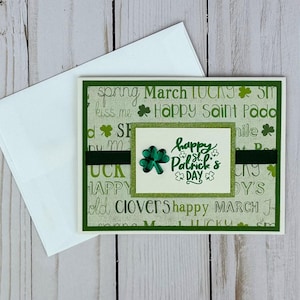 May include: A St. Patrick's Day greeting card with a white envelope. The card features a green and white background with the words "Happy St. Patrick's Day" and a shamrock. A dark green ribbon is across the card.