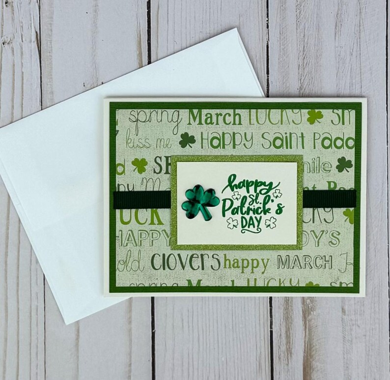 May include: A St. Patrick's Day greeting card with a white envelope. The card features a green and white background with the words "Happy St. Patrick's Day" and a shamrock. A dark green ribbon is across the card.