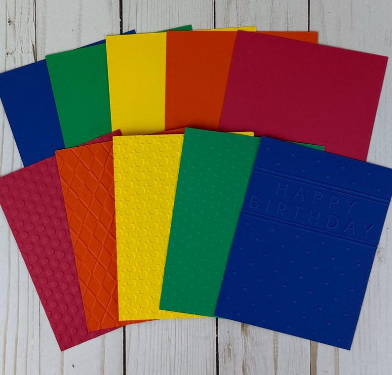 May include: A collection of colorful blank greeting cards in shades of red, orange, yellow, green, and blue. Some cards have textured patterns, while one blue card features the embossed text "HAPPY BIRTHDAY".