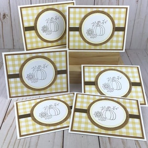 May include: A collection of six rectangular greeting cards featuring a yellow and white gingham pattern. Each card has a central circular white medallion with a black line drawing of a pumpkin and a sunflower, framed by a textured burlap border.
