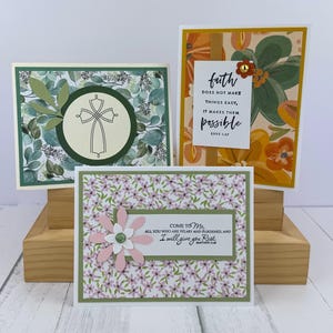 May include: Three handmade greeting cards. One features a cross design, another has floral patterns with the text "faith does not make things easy, it makes them possible", and the third has a flower with the text "Come to Me, I will give you Rest."