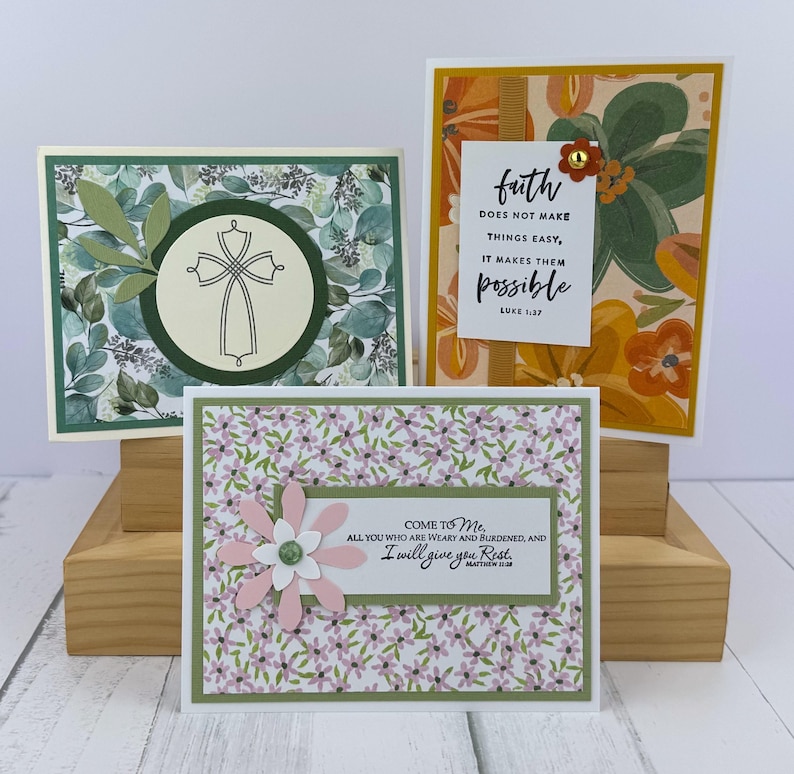 May include: Three handmade greeting cards. One features a cross design, another has floral patterns with the text "faith does not make things easy, it makes them possible", and the third has a flower with the text "Come to Me, I will give you Rest."