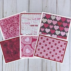 Puede incluir: Una colección de cinco tarjetas de felicitación cuadradas con varios diseños, incluyendo rosas rosas, el texto I LOVE YOU, corazones sobre fondo oscuro, rosas rojo oscuro, corazones de encaje blanco sobre rojo y rosas rojas con rejilla.