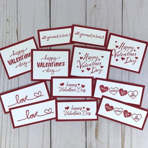 May include: A collection of Valentine's Day cards with red borders and white centers. The cards feature phrases like "Happy Valentine's Day," "All you need is love," and "Love," along with heart illustrations. Some cards also include "Sweet," "XOXO," "Luv Ya," and "Be Mine."