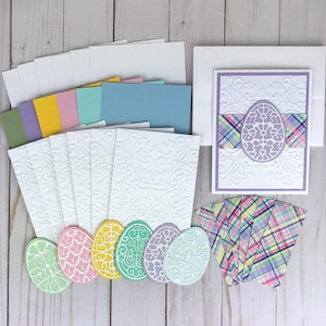 May include: A set of Easter card making supplies including white embossed cards, colorful patterned paper, and pastel colored die-cut eggs.