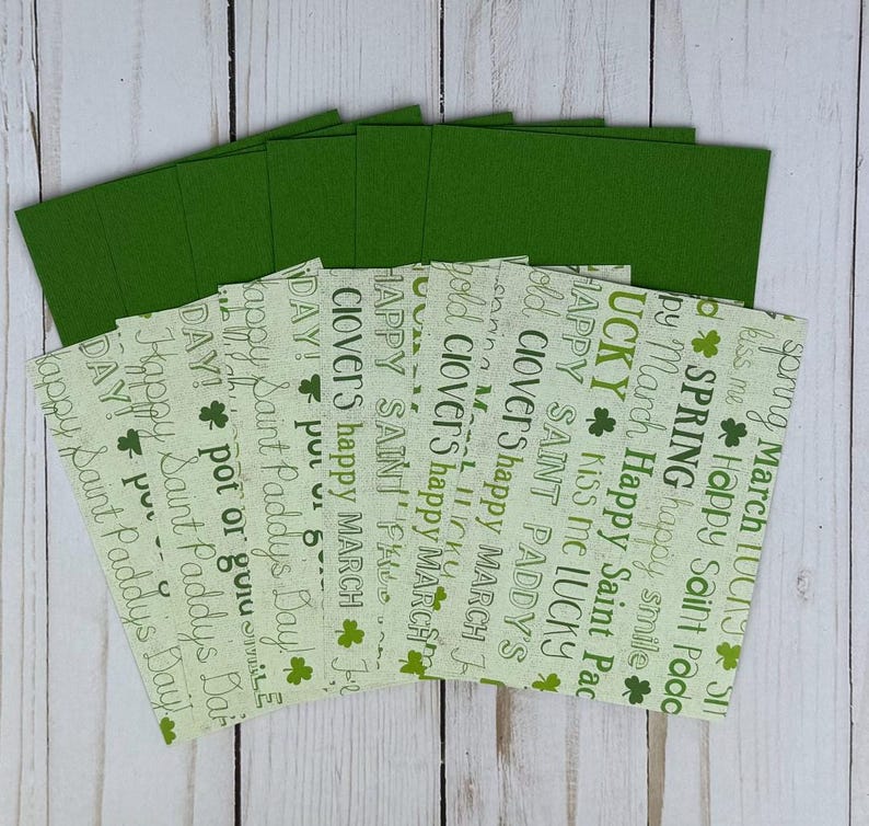 May include: A collection of green and patterned paper cards, likely for St. Patrick's Day. The patterned cards feature text like "Happy Saint Paddy's Day" and shamrock graphics. The solid green cards are stacked on top.
