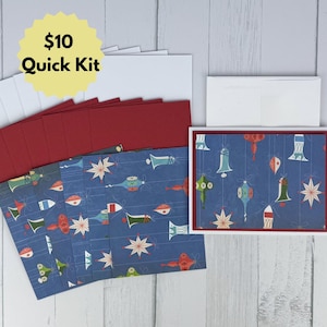 Puede incluir: Un juego de papelería con cartulina azul que presenta un patrón repetitivo de adornos navideños y estrellas colgantes en rojo, verde y blanco. El kit incluye varias tarjetas blancas en blanco, sobres de color rojo oscuro y sobres blancos.