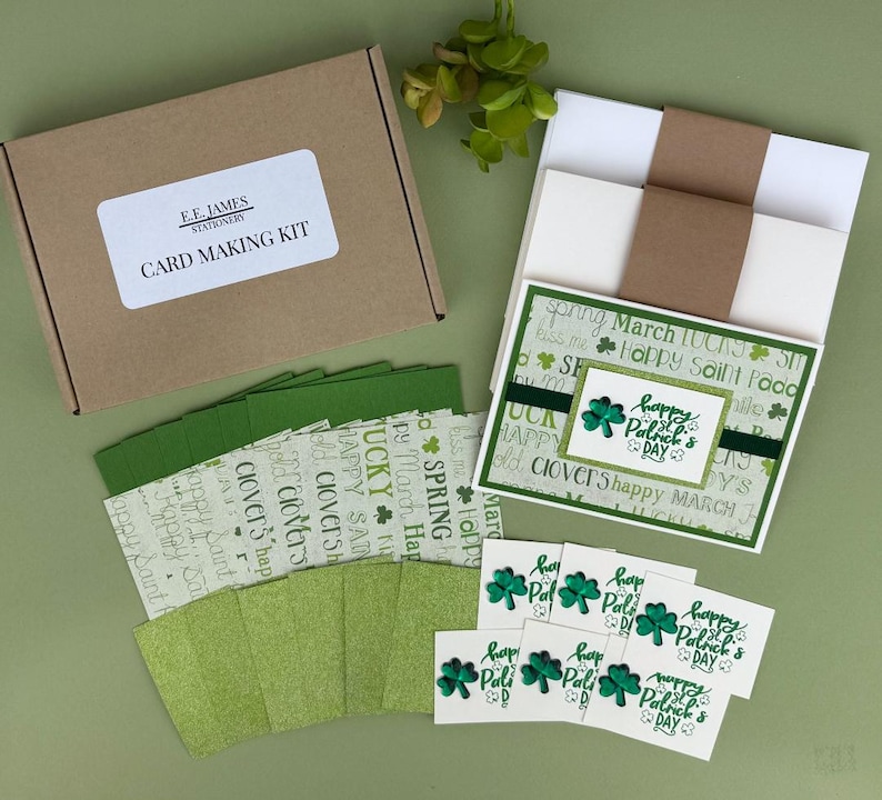 May include: A card-making kit with a brown box labeled "CARD MAKING KIT" and "E.E. JAMES STATIONERY." Includes green cardstock, patterned paper, and cards with shamrock designs and "Happy Patrick's Day" text. The kit is arranged on a green surface.