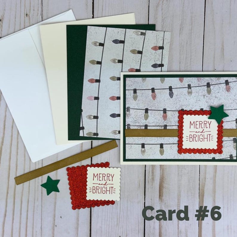 Puede incluir: Un juego de tarjetas de felicitaci&oacute;n con una tarjeta blanca con patr&oacute;n de luces, un cuadrado festoneado rojo, una cinta dorada y una estrella verde. La tarjeta muestra el texto MERRY and BRIGHT en rojo. Incluye sobres y cartulinas a juego.