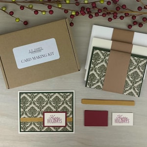 Puede incluir: Un kit para hacer tarjetas en una caja de cartón marrón con la etiqueta E.E. JAMES STATIONERY CARD MAKING KIT. Incluye sobres blancos y crema con bandas marrones, una tarjeta con estampado de damasco verde, cinta dorada y etiquetas Happy Holidays.