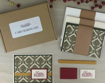 以下が含まれることがあります： E.E. JAMES STATIONERY CARD MAKING KITと書かれたラベル付きの茶色の段ボール箱に入ったカードメイキングキット。茶色の帯が付いた白とクリーム色の封筒の束、緑のダマスク柄のカード、金色のリボン、Happy Holidaysタグが含まれています。