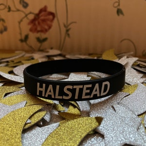 Puede incluir: Pulsera de silicona negra con la palabra "HALSTEAD" impresa en blanco.
