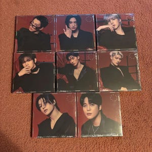 Peut inclure: Neuf albums CD scellés présentant des portraits d'hommes en tenue sombre sur fond rouge. Les pochettes d'album sont carrées et enveloppées dans du plastique transparent. L'esthétique générale est moderne et élégante.