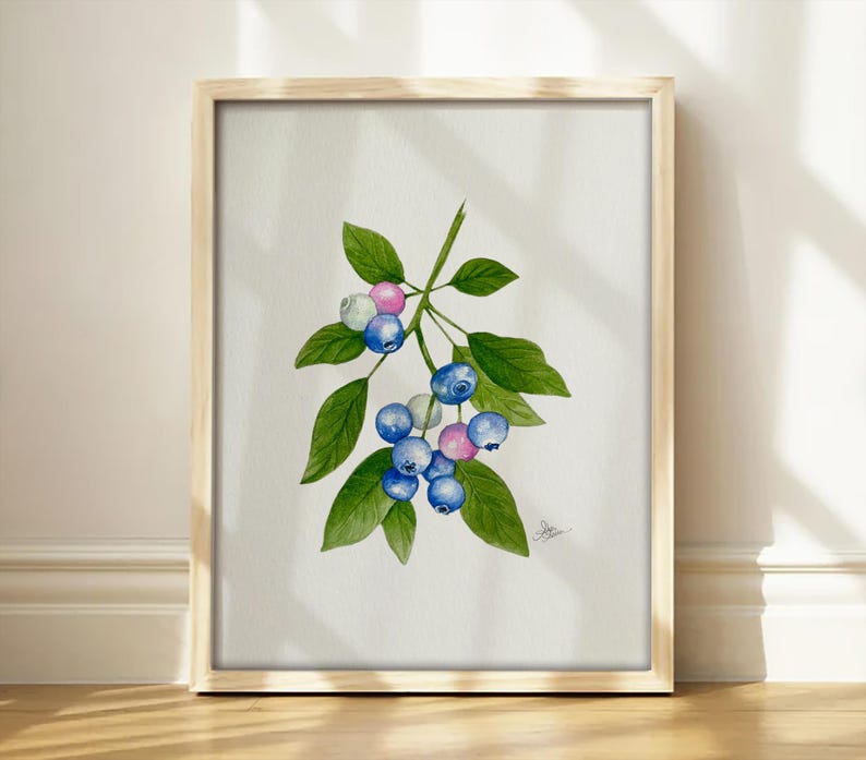 May include: A framed watercolor painting of a blueberry branch featuring several round blue and pink berries attached to green stems with pointed green leaves. The artwork is centered on a white background and includes a small signature in the corner.