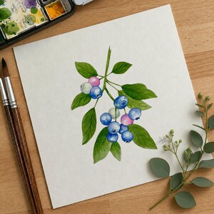 May include: A watercolor painting on white paper depicting a blueberry branch with green leaves and several round berries in shades of blue, light blue, and pink. The artwork features a signature in the bottom right corner and is rendered in a realistic style.