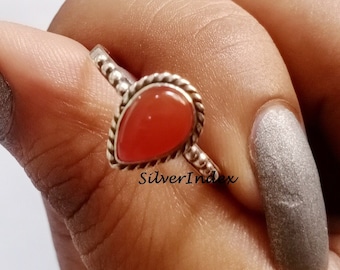 May include: A silver ring with a teardrop-shaped carnelian gemstone. The ring has a beaded band and a delicate design.