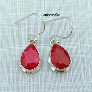 May include: A pair of silver teardrop earrings with red gemstone accents. The earrings have a simple, elegant design.