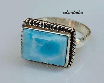 May include: A silver ring featuring a light blue rectangular gemstone set in a silver bezel with a rope-like border. The ring is on a white surface. "silverindex" is written in the upper right corner of the image.