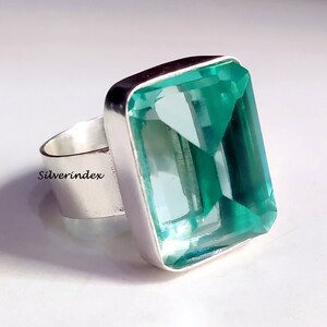 May include: A silver ring with a large, rectangular, light blue gemstone. The gemstone is faceted and has a clear, glassy appearance.
