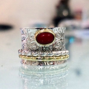 May include: A silver and gold spinning ring with a red gemstone. The ring has a decorative, swirling pattern.