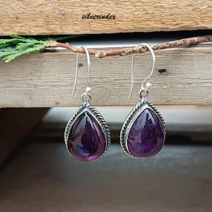 May include: A pair of silver drop earrings with teardrop-shaped, deep purple amethyst stones. The stones are set in a silver frame with a twisted rope design. The earrings hang from silver hooks. The word "silverindex" is visible in the image.