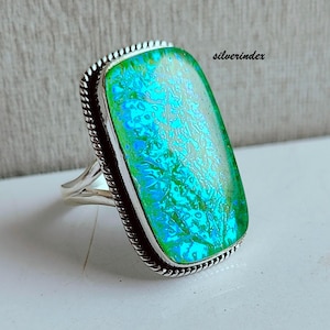 May include: A silver ring with a large, rectangular, iridescent green and blue stone. The stone has a textured, patterned appearance. The ring has a twisted rope design around the stone and a split band. The word "silverindex" is visible on the image.
