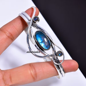 May include: Silver cuff bracelet with a large oval blue labradorite gemstone and two smaller round labradorite gemstones. The bracelet has a delicate, intricate design.