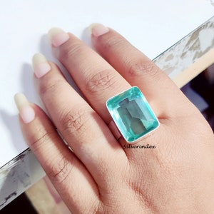 May include: A silver ring with a large, rectangular, light blue gemstone. The ring is on a person's finger.