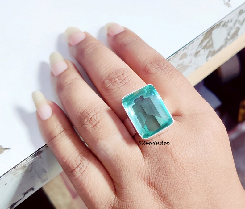 May include: A silver ring with a large, rectangular, light blue gemstone. The ring is on a person's finger.