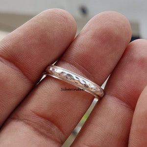 May include: A silver hammered band ring. The ring is worn on a finger.