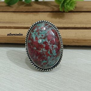 May include: A silver ring with a large oval red and green gemstone set in a twisted silver band.