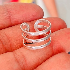 May include: A silver-colored ring with a unique design. The ring features three horizontal bands connected by vertical loops. The text "silverindex" is visible on the ring. The ring is designed to be worn on a finger.