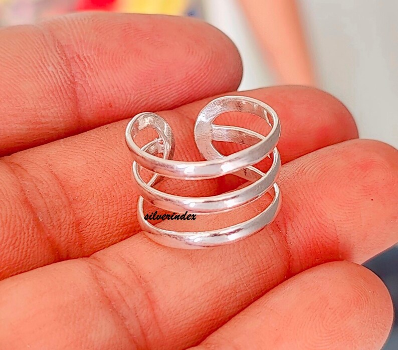 May include: A silver-colored ring with a unique design. The ring features three horizontal bands connected by vertical loops. The text "silverindex" is visible on the ring. The ring is designed to be worn on a finger.