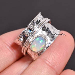 May include: A silver spinning ring with a white opal gemstone. The ring has a hammered texture and a band that spins freely.